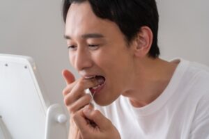 鏡の前で奥歯にフロスを通している男性の写真